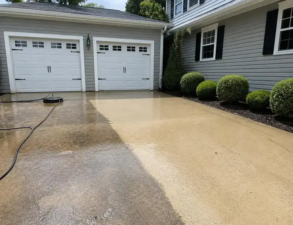 Concrete driveway being pressure washed beside a clean residential home exterior